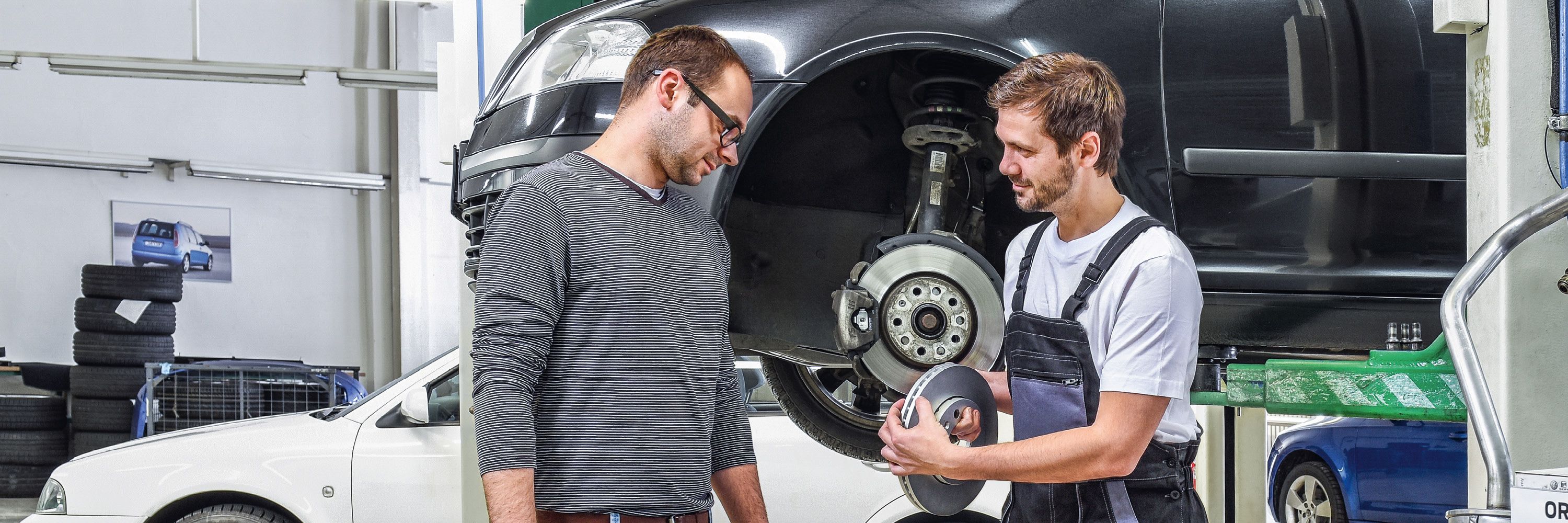 Ein Škoda Mechaniker in der Werkstatt zeigt einem Kunden die Bremsscheiben